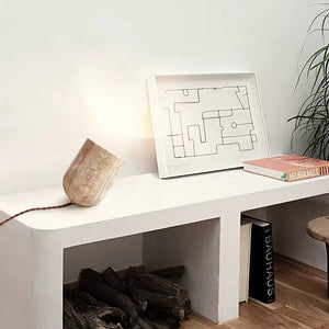Minimalist white bench with a sculptural Natural Stone Lamp featuring yellow cave stone, a framed abstract line drawing, books including “BAUHAUS” and “NEUBAULEIT,” and firewood stored underneath.
