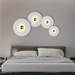 A neatly made bed with white bedding sits against a gray wall, above which four Origami Circle Wall Lights are arranged in an arc, casting a soft glow that enhances the serene atmosphere.