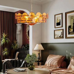 A modern living room featuring an Italian Retro Pendant Light in vibrant orange, a beige sofa, round coffee table with a plant, framed wall art, and a floor lamp beside the seating area.
