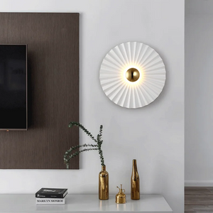 A modern living room wall featuring the Origami Circle Wall Light, part of a TV screen, and a white shelf with gold decorative items and a plant.