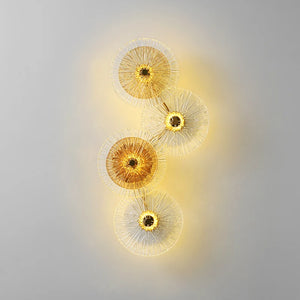 Four Amber Deco Wall Sconce lights, featuring nature-inspired circular designs with radiating spokes, emit warm yellow light against a plain gray background, seamlessly blending organic style with modern elegance.