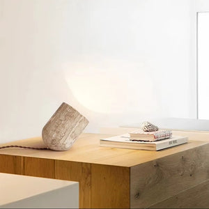A Natural Stone Lamp, two books, and a seashell rest on a light wood table in a minimalist, well-lit room with white walls.