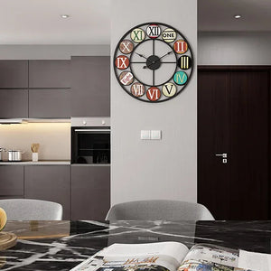 A modern kitchen and dining area with grey cabinets features the Nordic Color-Ring Wall Clock, which displays vibrant Roman numerals and the word "ONE" for the number 1.