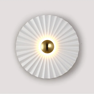 The Origami Circle Wall Light features a round LED design with a pleated white shade and a central metallic gold disk, making it a perfect gold accent wall light for any space.