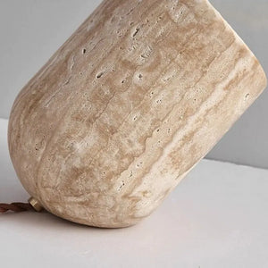 A close-up of a beige, stone-textured cup with a rounded shape, resting on its side on a light gray surface—its organic finish reminiscent of the Natural Stone Lamp.