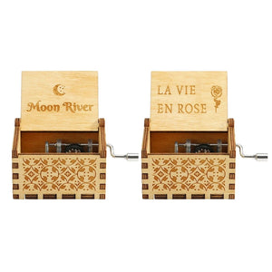 Two Wooden Music Boxes with ornate designs. The left one is labeled "Moon River" and the right one "La Vie En Rose" with a rose engraving. Both are Wooden Music Boxes, handmade and featuring hand-crank mechanisms that play classic tunes.