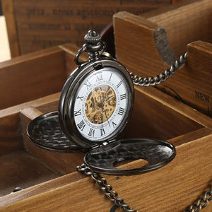 The Vintage Mechanical Pocket Watch, featuring Roman numerals and a visible movement, rests open on a wooden box and is attached to a metal chain.