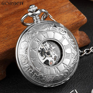 The Vintage Mechanical Pocket Watch, featuring ornate engravings, Roman numerals, and a silver finish with visible gears beneath a glass center, rests on a wooden surface.