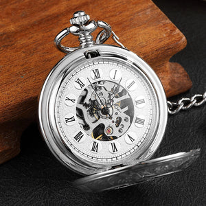 A Vintage Mechanical Pocket Watch with Roman numerals and exposed gears rests on a black surface next to a wooden object.