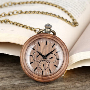 A Handmade Antique Vintage Pocket Watch Custom Bronze Quartz Walnut Wooden Pocket Watch with a chain rests against an open book on a wooden surface.