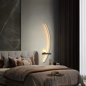 Modern bedroom with a neutral color scheme, featuring a bed with multiple pillows, an elegant Arc Wall Sconce for stylish lighting, a small round side table, and floor-to-ceiling curtains.