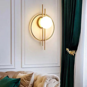 A Circular Wall Sconce with Dual Vertical Rods, mounted on a paneled white wall, near a green curtain and a beige tufted sofa with pillows.