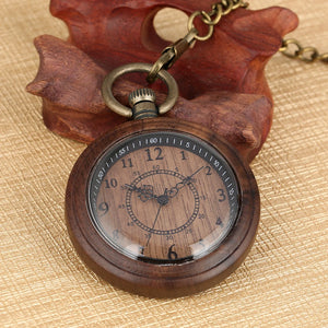 The Wooden Pocket Watch features black numerals and ornate hands on a round wooden face, displayed on a carved leaf-shaped wooden holder atop a textured beige surface.