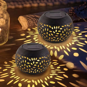Two Solar Orb Lamps with cutout patterns project intricate light designs onto a surface in a dimly lit setting, while a jar candle and fabric appear in the background.