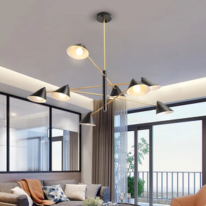 A modern living room showcases a sleek Multi-Arm Ceiling Light in black and gold, accompanied by a sectional sofa with plush cushions. Large windows lead to a balcony featuring a potted plant.