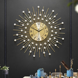 The Lux Radiance Starburst Wall Clock, featuring a large gold design with white accents, is mounted on a dark wall above a dining table set with blue dinnerware, serving as a striking statement piece.