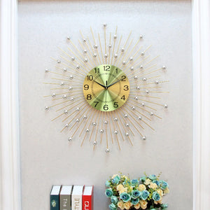 A Lux Radiance Starburst Wall Clock hangs above a small shelf displaying books and a bouquet of artificial flowers.