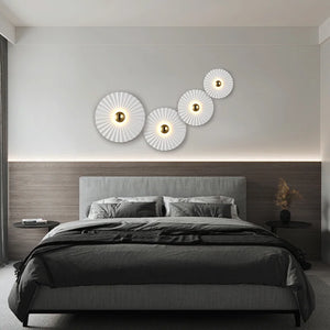 A modern bedroom featuring a gray upholstered bed, wooden accent wall, minimalist bedding, and four Origami Circle Wall Lights arranged above the headboard.