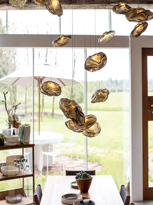 A dining area with a wooden table, ceramic dishes, and the Luxe Cloud Glass Pendant Light with textured glass, set against large windows overlooking a green outdoor space.