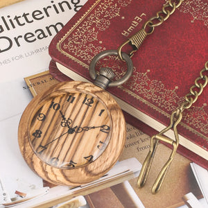 A Wooden Pocket Watch from the collection is displayed on an open magazine and a red embossed journal.