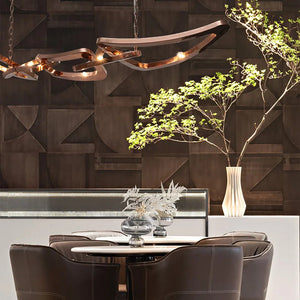 A modern dining area with a round table, leather chairs, an Elegant Industrial Gallery Pendant, and a vase with green branches set against a geometric dark wall.