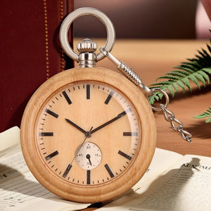 The Wood Pocket Watch, featuring a metal chain, sits on an open book with a fern and a closed red book in the background.