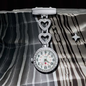 The Luxe Fob Pocket Watch with heart-shaped links and rhinestones rests on a striped fabric background, accented by a small star-shaped brooch nearby.