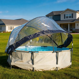 A large outdoor above-ground pool with a clear dome cover stands on a grassy lawn in front of suburban houses under a blue sky.