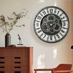 An Industrial Gearworks Wall Clock with exposed gears hangs above a wooden dresser topped with a vase of dried branches, books, and a modern sculpture.