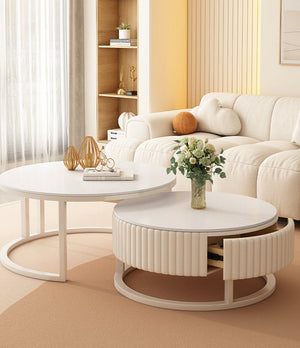 The Luxury Round Coffee Table Set, featuring two modern white tables—one with a ribbed drawer—stands in a living room with a cream sofa, a vase of flowers, and gold decorative sculptures.