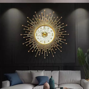 The Premium Sun Wall Clock with gold spokes hangs on a dark wall above a modern sofa with cushions, next to a small potted plant.