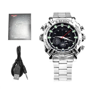 The Watch SpyCam, shown with its USB cable and manual on a white background, is a silver wristwatch with multiple buttons that discreetly records 1080P video and audio for enhanced security and convenience.
