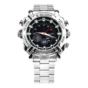 The Watch SpyCam is a silver wristwatch with a black round face, labeled bezel buttons, "G-SKOOH" at the top, and a polished stainless steel band. It discreetly records 1080P video and audio with a hidden camera.