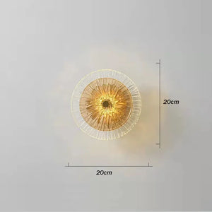 The Amber Deco Wall Sconce is a round, nature-inspired light measuring 20cm by 20cm, shown glowing elegantly against a simple grey background.