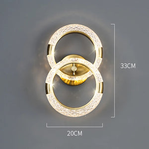 The Elegant Ring Wall Sconce is a luxurious wall light fixture featuring two interlocking illuminated rings, with dimensions of 33 cm in height and 20 cm in width. The gold-colored rings and base add an elegant touch to any space.