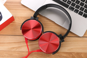 A pair of Wired Bass Headphones in red, featuring an ergonomic design and a red cable, are placed beside a laptop on a wooden surface.