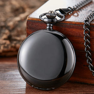The Vintage Mechanical Pocket Watch, closed and attached to a chain, rests on a wooden box, its smooth silver finish reflecting light.