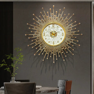 The Premium Sun Wall Clock with a gold sunburst design and decorative face hangs above a dining table with chairs, lush plants, and tableware in a modern room.