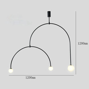 The Minimalist Line Light is a modern pendant featuring two curved black arms, each ending with a spherical bulb. Its sleek design embodies contemporary elegance with a subtle mounting system and dimensions of 1200mm in height and width against a sophisticated gray backdrop.