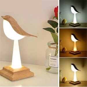 The Bird Table Night Light showcases elegant craftsmanship in a contemporary design. Illuminated with soft light, it is displayed both unlit and lit from various angles. A rose in a glass jar sits gracefully to the left.
