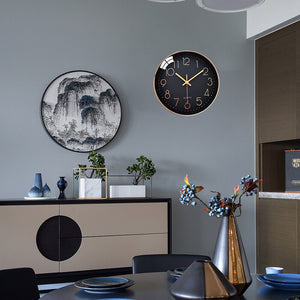 A modern dining room features a round black wall clock, specifically the Wall Clock SpyCam with motion detection, and a landscape painting on a gray wall. A sideboard displays vases, while the table is set with blue dinnerware and a metallic vase with flowers. The room feels high-tech yet cozy.