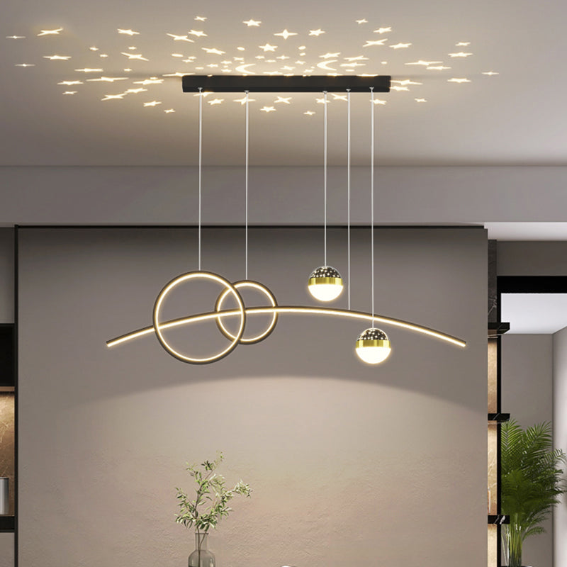 The Stellar Pendant Light features circular and linear elements that create star-shaped patterns with celestial accents when hung from the ceiling. A green plant can be seen in the background.