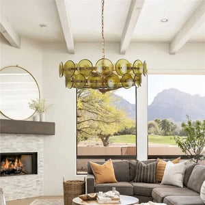 A modern living room with a gray sectional sofa, an Italian Retro Pendant Light with yellow glass discs, a fireplace, and large windows framing mountain scenery.