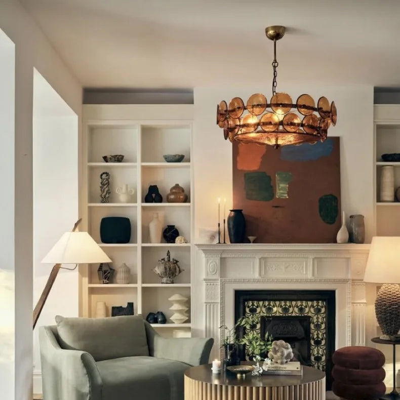 A living room with an armchair, round coffee table, built-in shelves, ornate fireplace, abstract painting, and an elegant Italian Retro Pendant Light.
