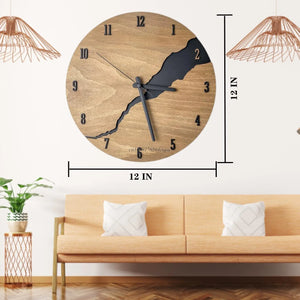 Displayed in a living room adorned with a minimalist light-colored sofa and decorative plants, the Wooden Round Wall Clock features black hands and a distinctive river-like design. Its natural wood finish enhances its rustic charm, while its dimensions are 12x12 inches.