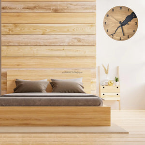 A minimalist bedroom featuring a wooden bed, gray bedding, and the Wooden Round Wall Clock in a rustic modern style. A small nightstand with a plant sits beside the bed. The room showcases wood paneling and floors with a natural wood finish.