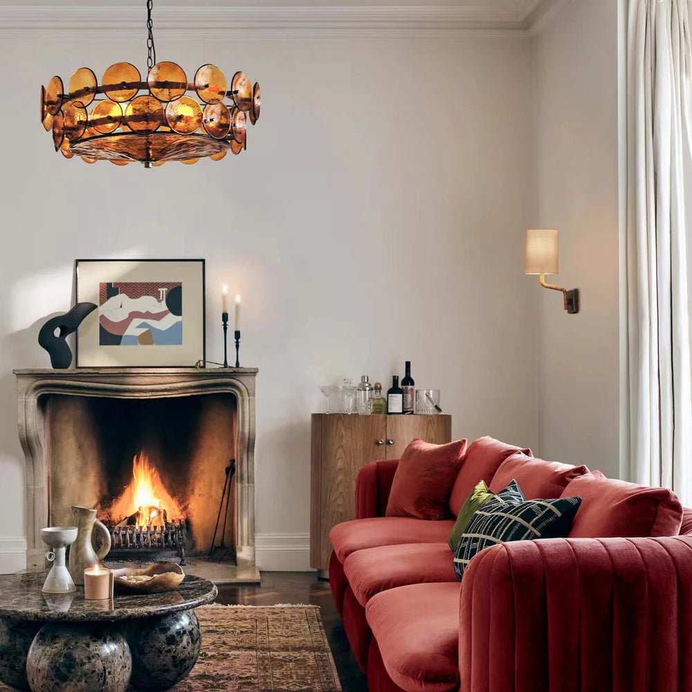 A living room with a lit fireplace, red velvet sofa, round coffee table, sideboard with bottles, abstract art, and an eye-catching Italian Retro Pendant Light.