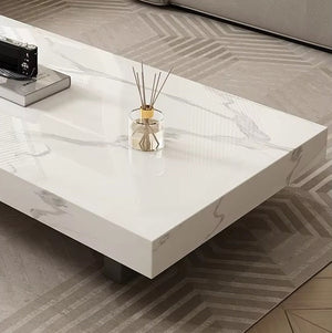 The Modern Luxe Coffee Table, a white rectangular piece with subtle gray veining, holds a glass reed diffuser and sits on a patterned rug by a light-colored sofa, bringing elegance to modern interiors.