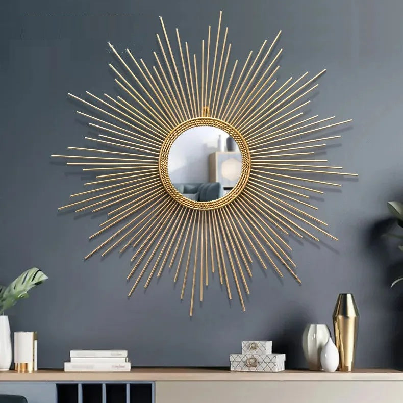 The Luxe Sunray Wall Mirror, featuring a gold metal frame and large round design, serves as a striking statement piece above a modern console table with decor accents on a dark gray wall.