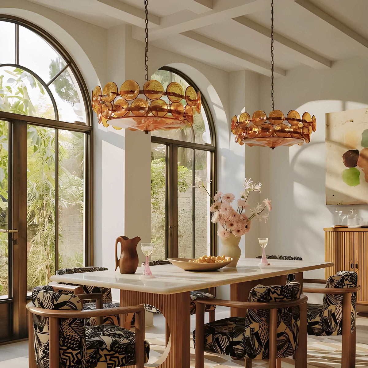 Sunny dining room with large arched windows, a white table, patterned chairs, two Italian Retro Pendant Lights, a vase of flowers, and glassware set on the table.